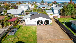 A residential area with a large house featuring a covered patio, a brick driveway, and a view of a body of water. - Central Inn Taupo (Taupo)