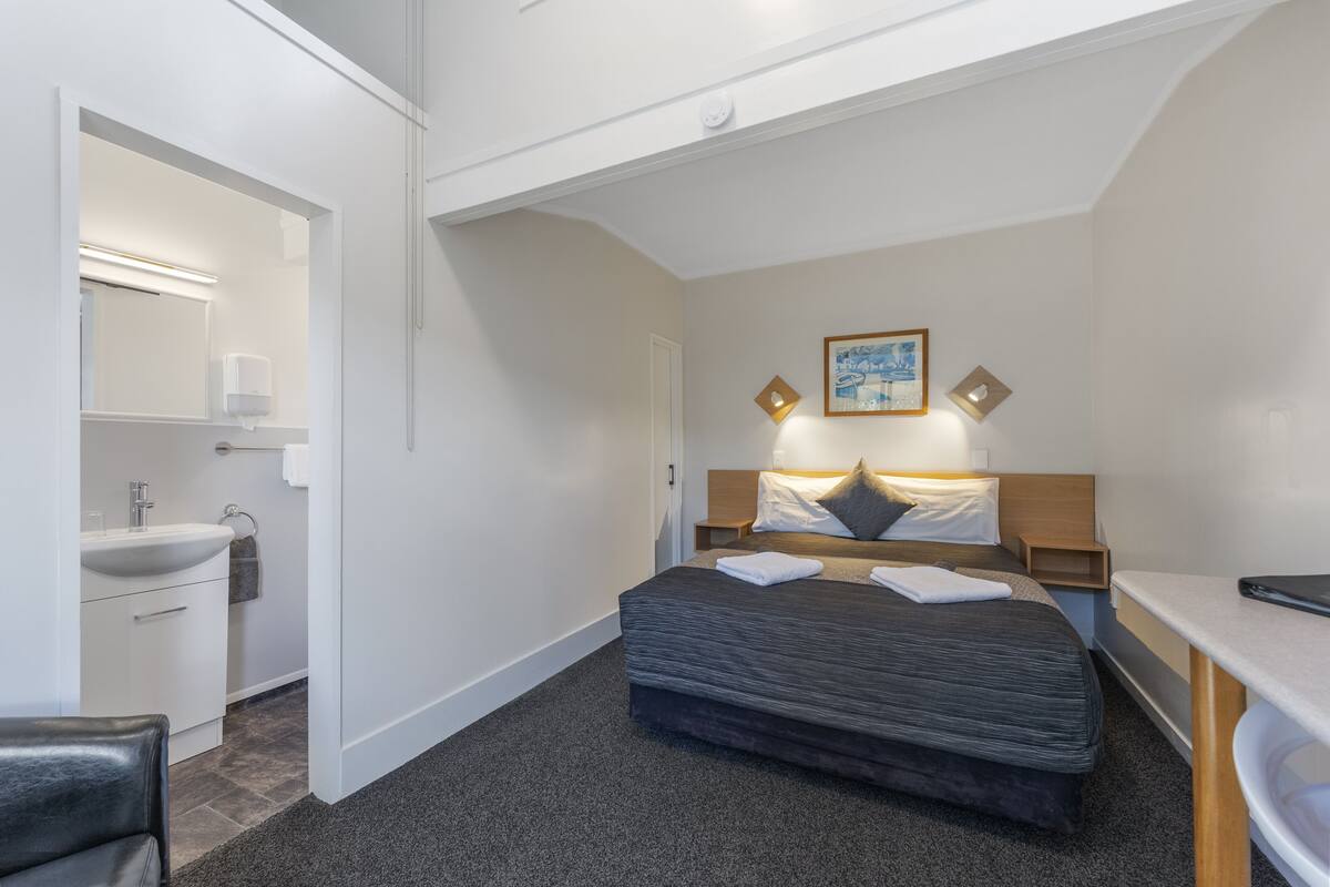 Ein modernes Hotelzimmer mit einem großen Bett, Nachttischen, einem Schreibtisch und einem Badezimmer mit Waschbecken und Spiegel.