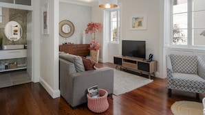 Ein modernes Wohnzimmer mit einem grauen Sofa, einem Fernseher, einem gemusterten Sessel und einer Holzkommode.
