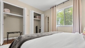 Un dormitorio con cama, armario abierto, ventana con cortinas y vista a árboles desde el exterior.