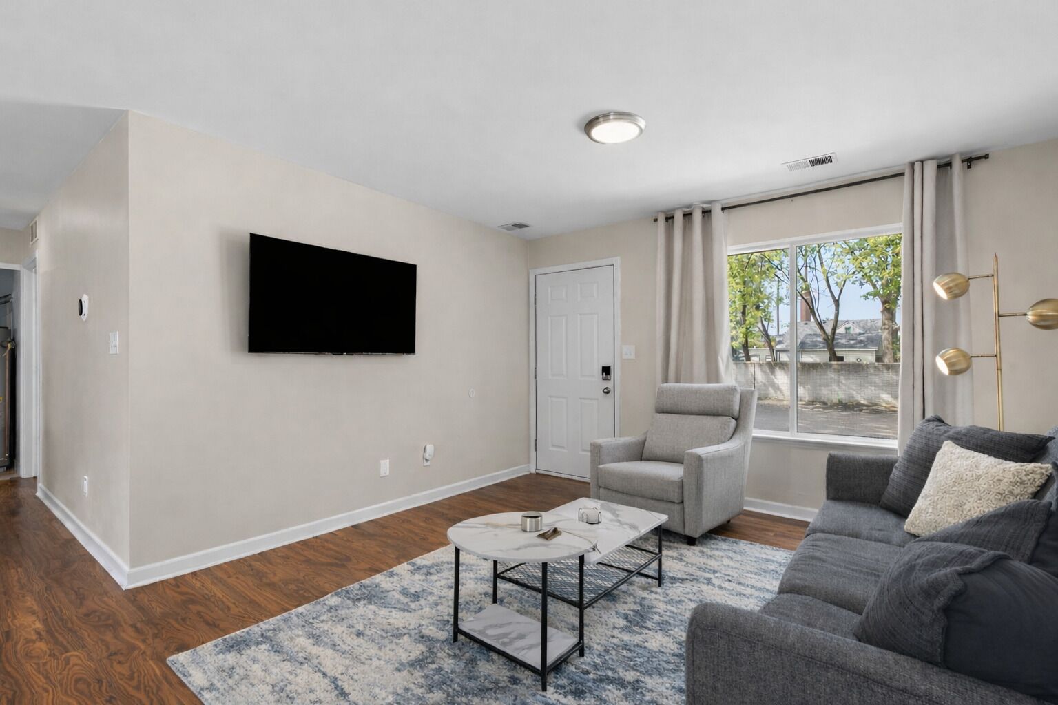 A modern living room with a flat-screen TV mounted on the wall, a grey armchair, a grey sofa, and a coffee table.