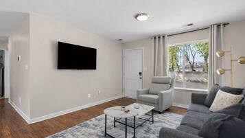 A modern living room with a flat-screen TV mounted on the wall, a grey armchair, a grey sofa, and a coffee table.