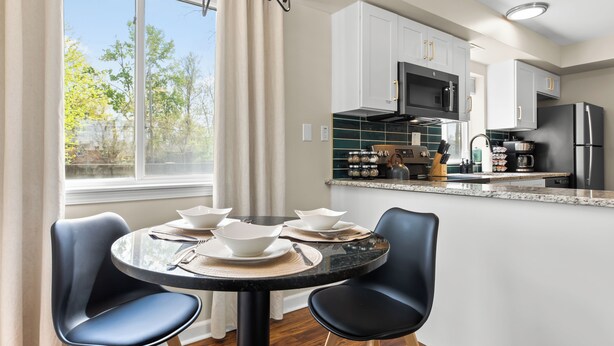 Una cocina moderna con armarios blancos, un refrigerador negro y un comedor con dos sillas y una mesa dispuesta para cuatro.