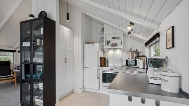 A modern kitchen with white cabinetry, a black-framed glass cabinet, a stainless steel sink, and a coffee machine.