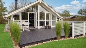 A modern house with a large glass front, a wooden deck, and a chimney.