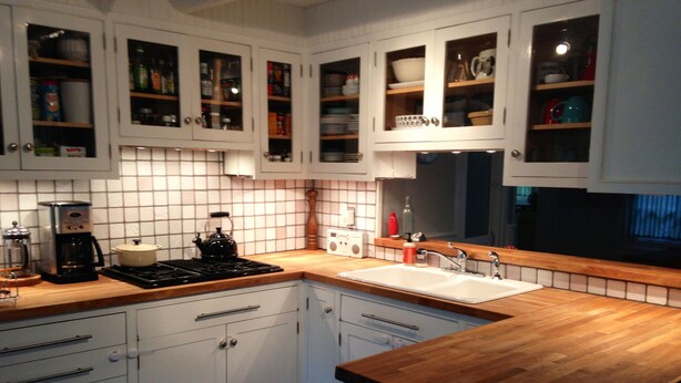 Een moderne keuken met witte kasten, een houten aanrecht, een fornuis, een koffiezetapparaat en een spoelbak.