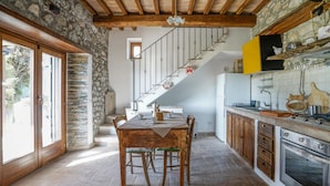 A rustic kitchen with a stone wall, wooden beams, a staircase, and a dining area with a table and chairs. - Pet friendly home in Campiglia D'orcia (Campiglia D'orcia)