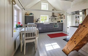A kitchen with a white dining table, grey cabinets, a red rug, and a wooden bench.