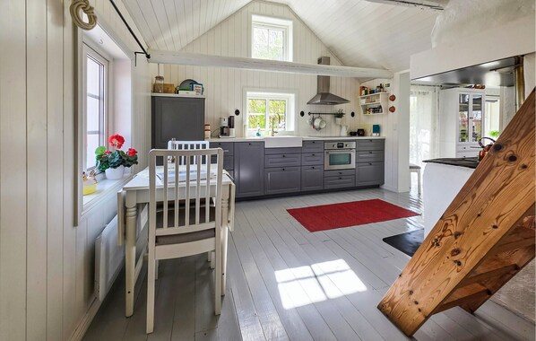 A kitchen with a white dining table, grey cabinets, a red rug, and a wooden bench.