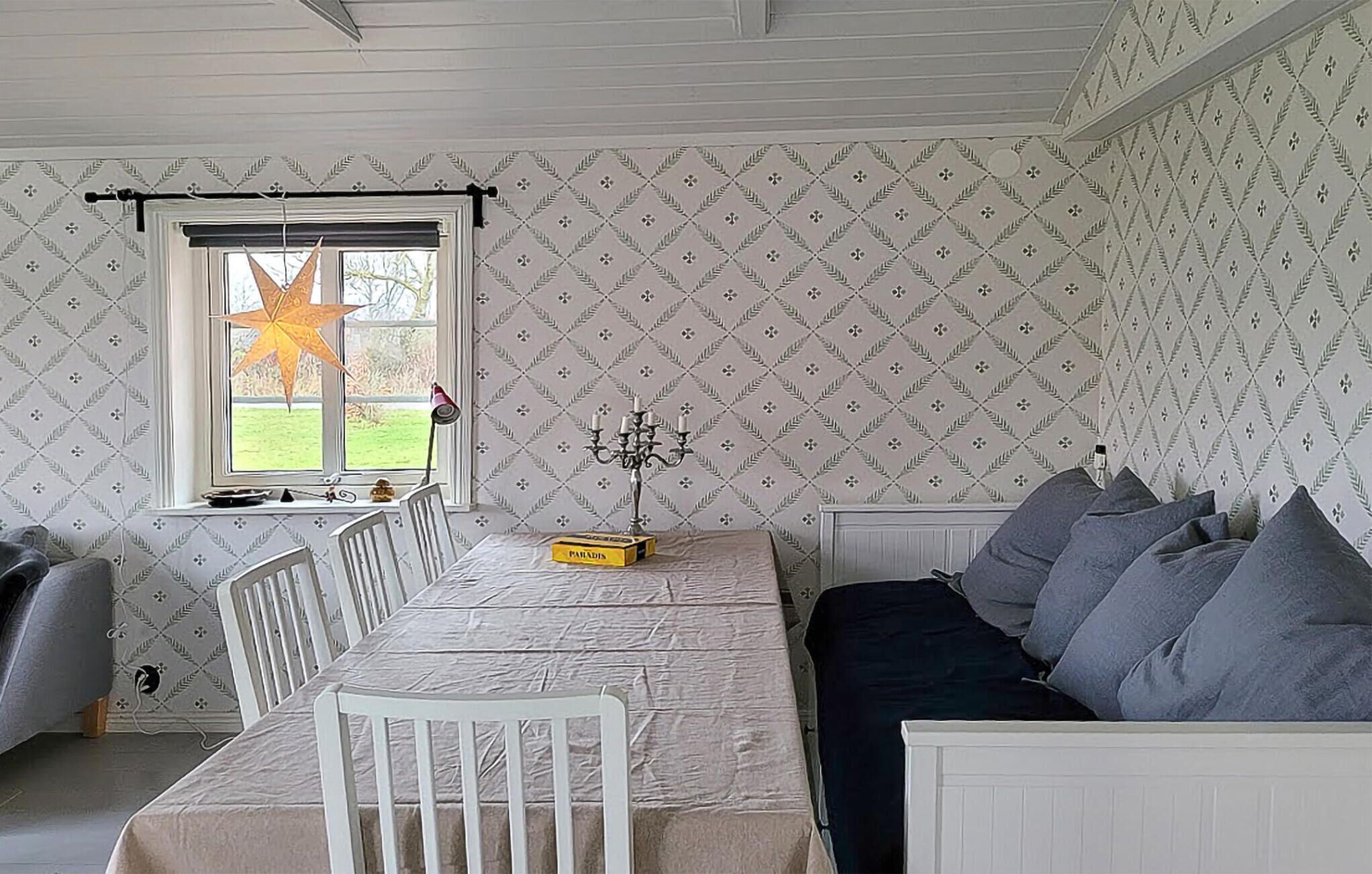 A room with a dining table, chairs, a sofa, a window with a star decoration, and patterned wallpaper.