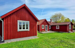A red wooden building with a white window, a chimney, and a small porch.