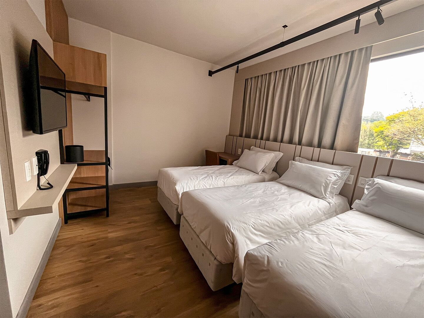 Une chambre d’hôtel avec deux lits, un téléviseur fixé au mur et une fenêtre avec des rideaux.
