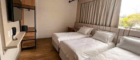 A hotel room with two beds, a TV mounted on the wall, and a window with curtains.