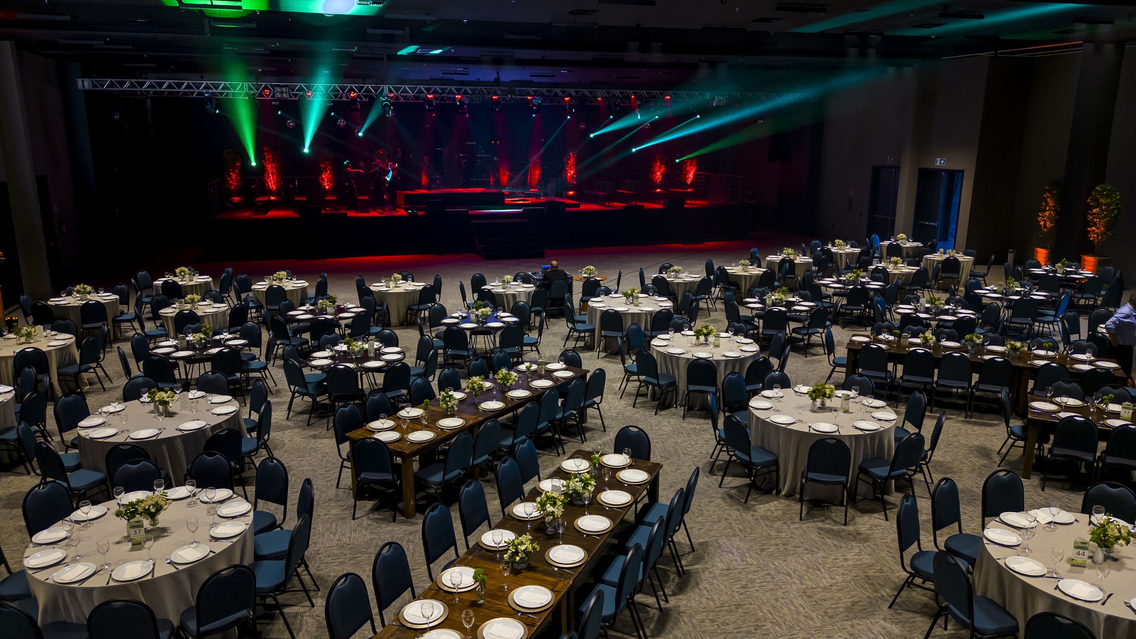 Un salón de banquetes con mesas redondas dispuestas para comer, un escenario con iluminación y suelo alfombrado.