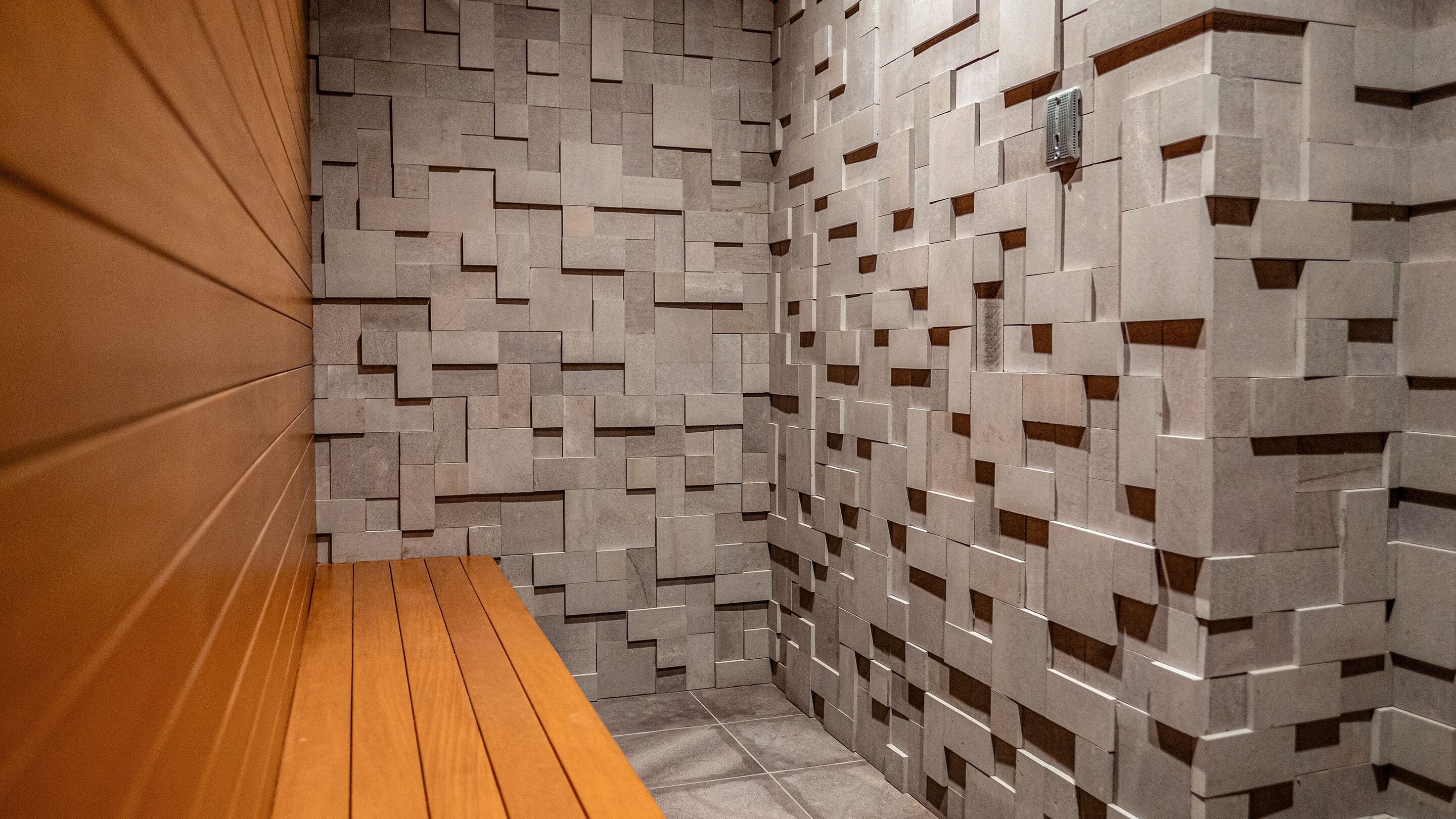 Un bagno moderno con un muro a motivi geometrici, una panca in legno e un asciugamani ad aria.