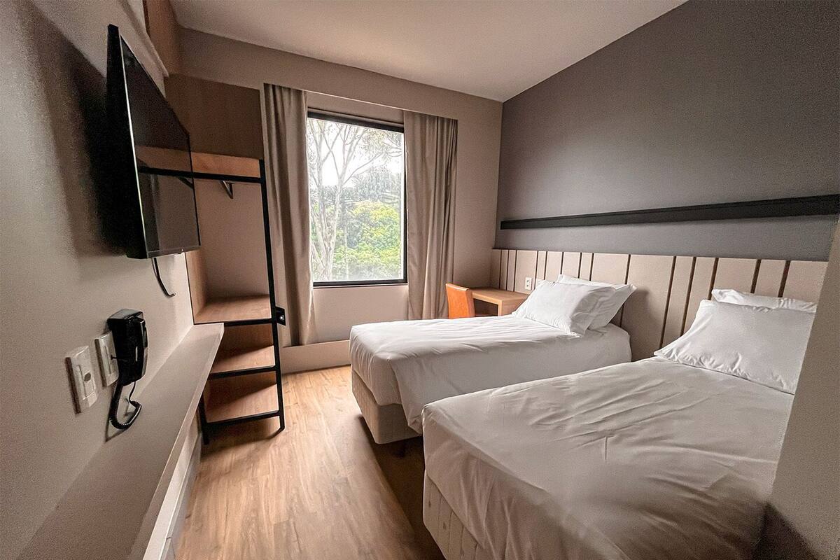 Habitación de hotel con dos camas, un televisor montado en la pared, piso de madera y una ventana con cortinas.