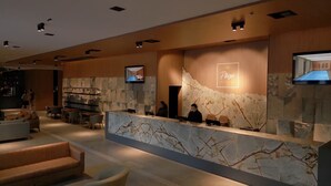 Un área de recepción moderna con mostrador de mármol, asientos y una pantalla de televisión que muestra 'Plaza'.
