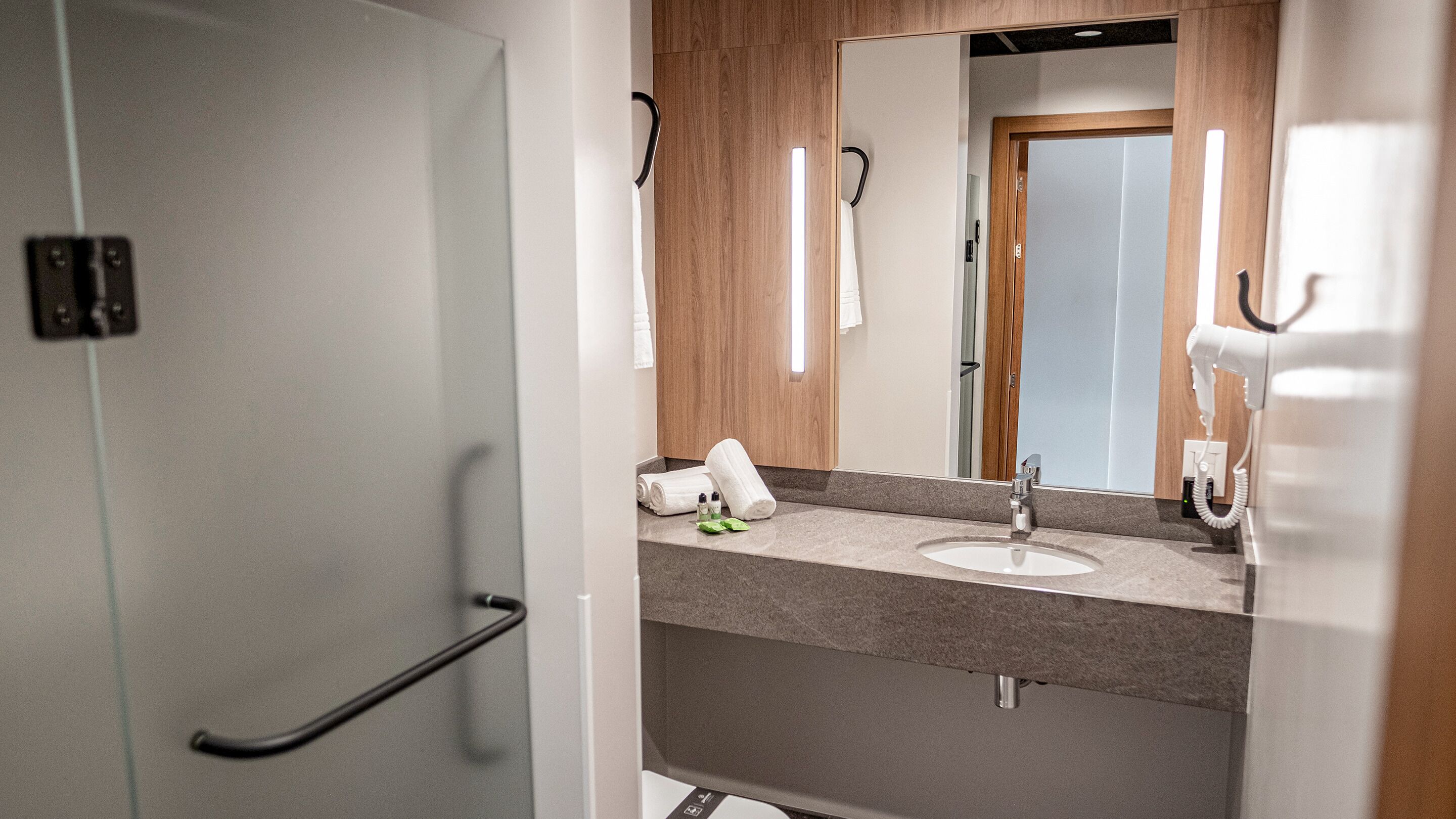 A modern bathroom with a grey sink, wooden vanity, and a mirror.