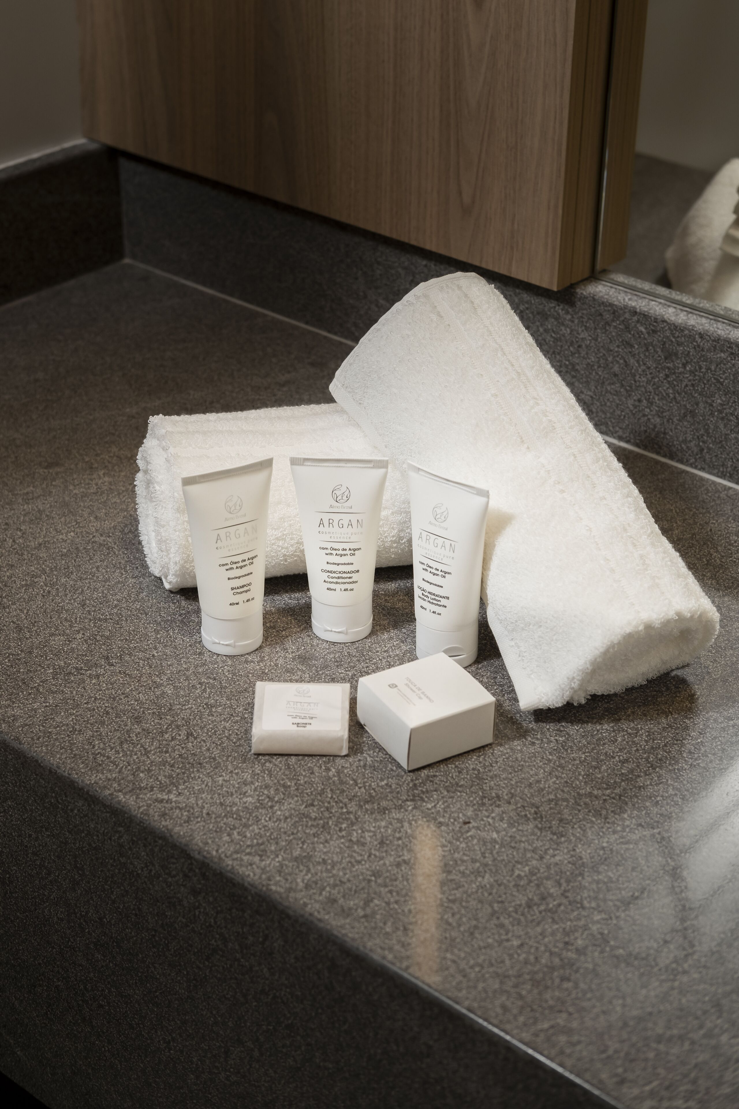 Una encimera de baño con una toalla blanca, dos botellas de productos capilares de Argán y dos cajas pequeñas.