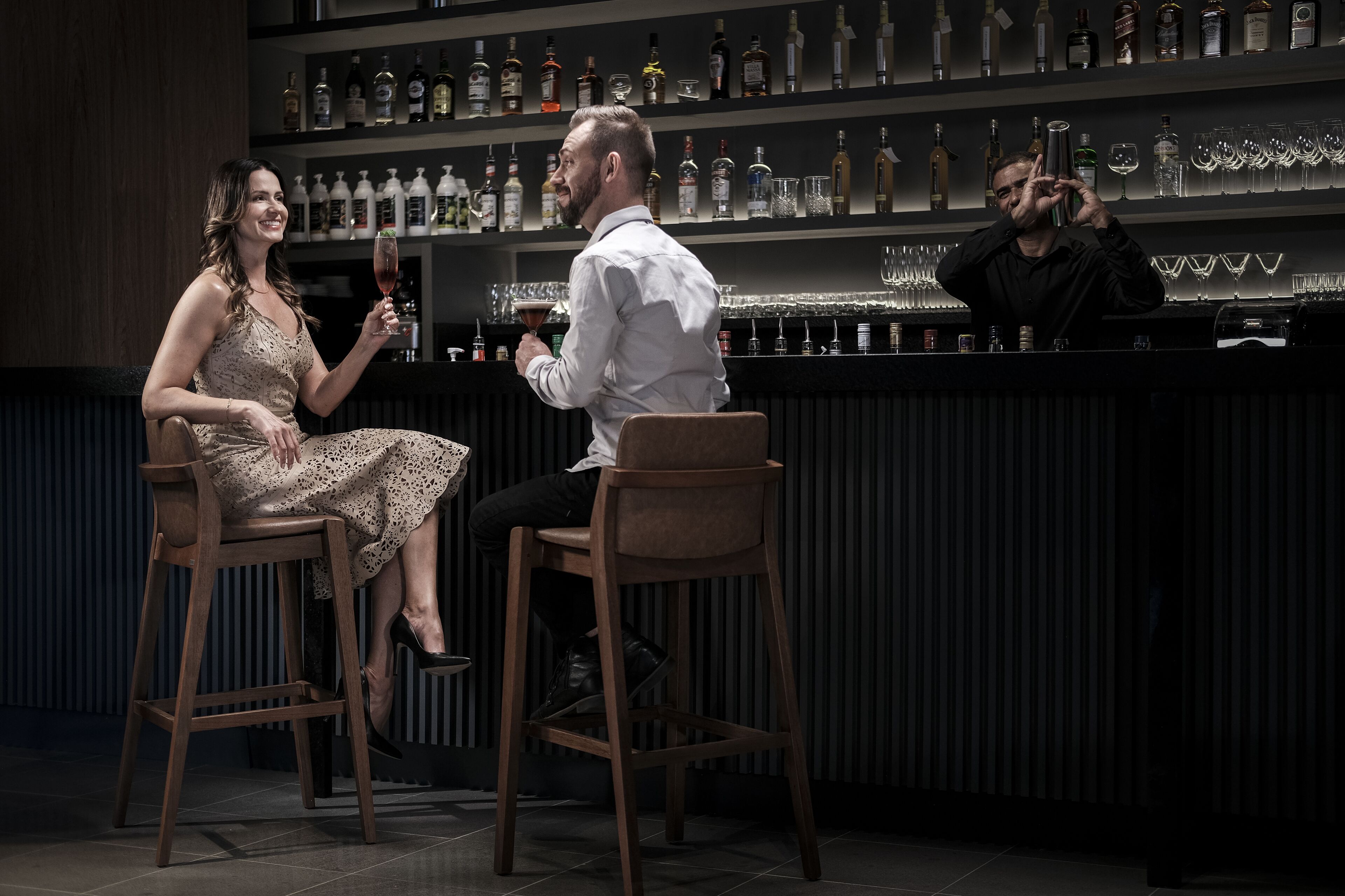 A bar area with stools, a bartender, and shelves of liquor bottles.