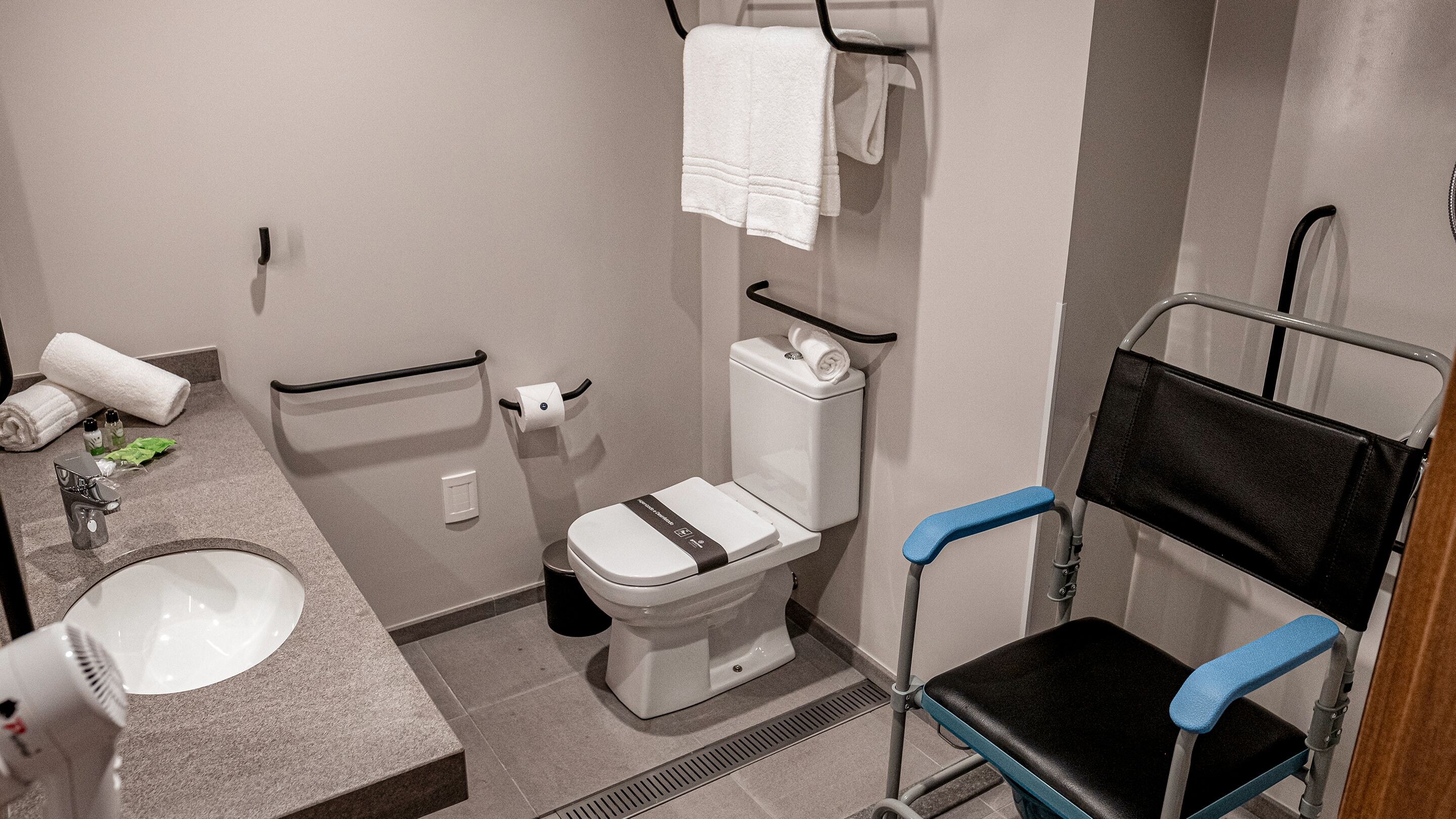 A modern bathroom with a toilet, sink, and a wheelchair-accessible chair.