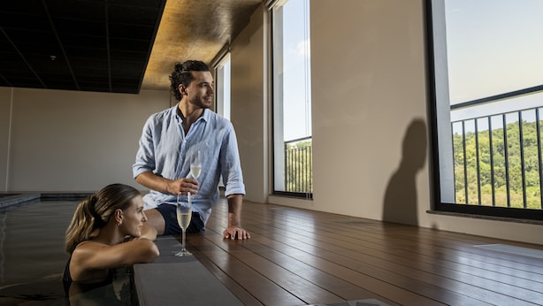 Una habitación con piso de madera, ventanas amplias y un balcón con vista a zonas verdes.
