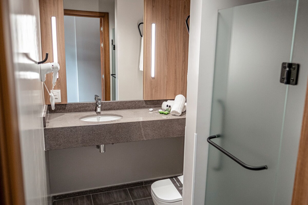 Een moderne badkamer met een wastafel, spiegel, handdoekrek en een douchecabine van glas.