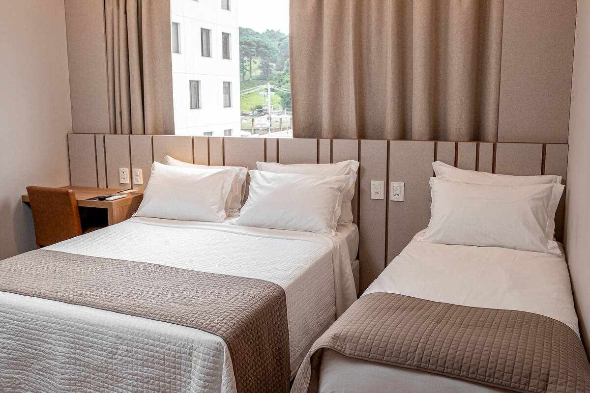 Una habitación de hotel con dos camas, una mesita de noche de madera, un escritorio y una ventana con cortinas.