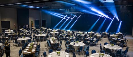 Un amplio salón de conferencias con varias mesas redondas dispuestas para comer, equipado con sillas y mantelería.