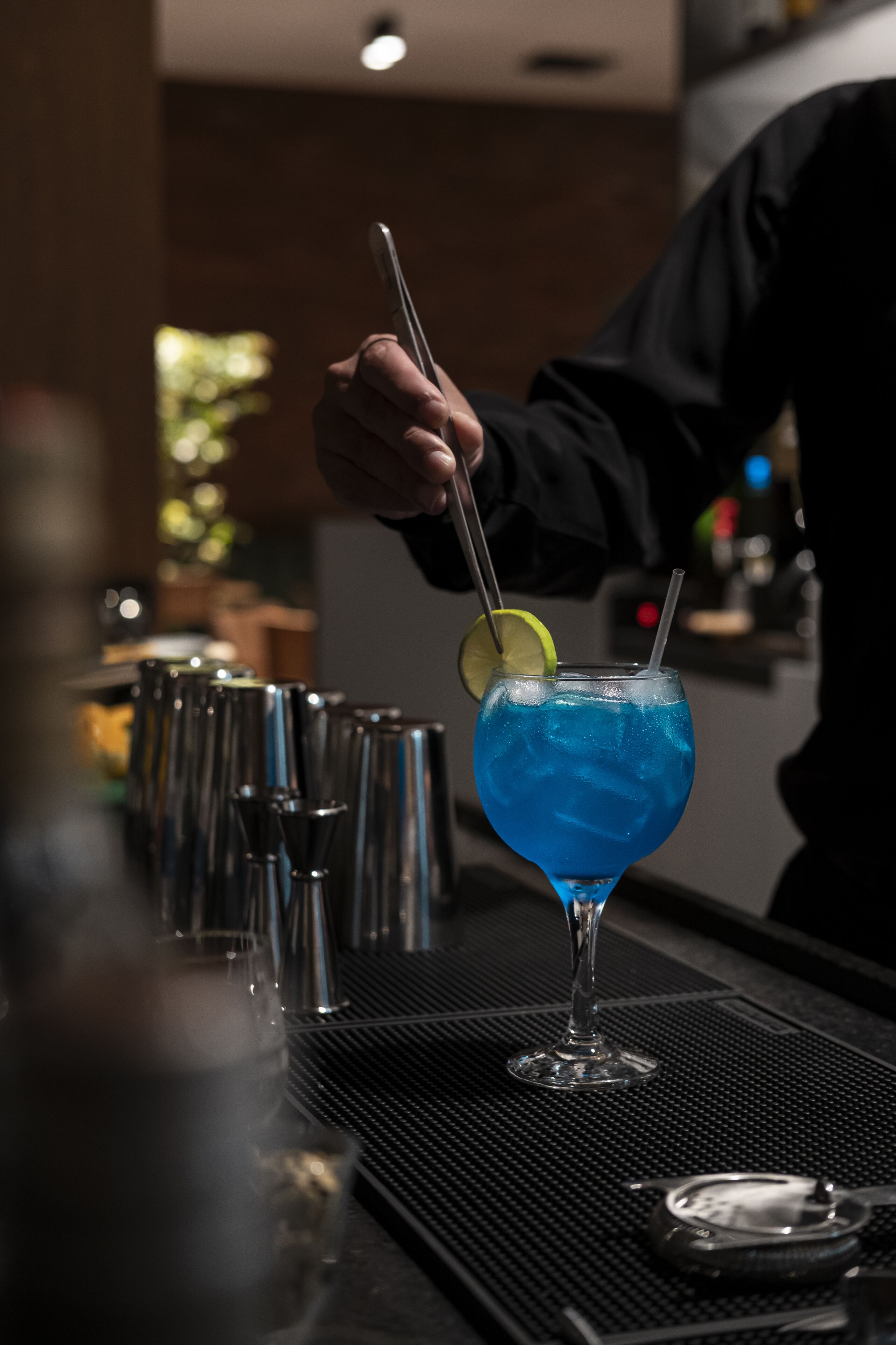 A bar setting with a blue cocktail, a lime wedge, and a straw.