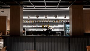 Zona de bar con un bartender preparando bebidas, estantes con botellas y un diseño de interiores moderno.