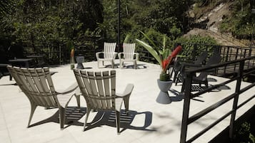 An outdoor patio with chairs and tables, surrounded by lush greenery and a view of a hillside.