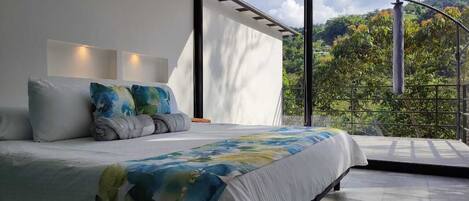 Een slaapkamer met een groot bed, uitzicht op groen en een balkon.