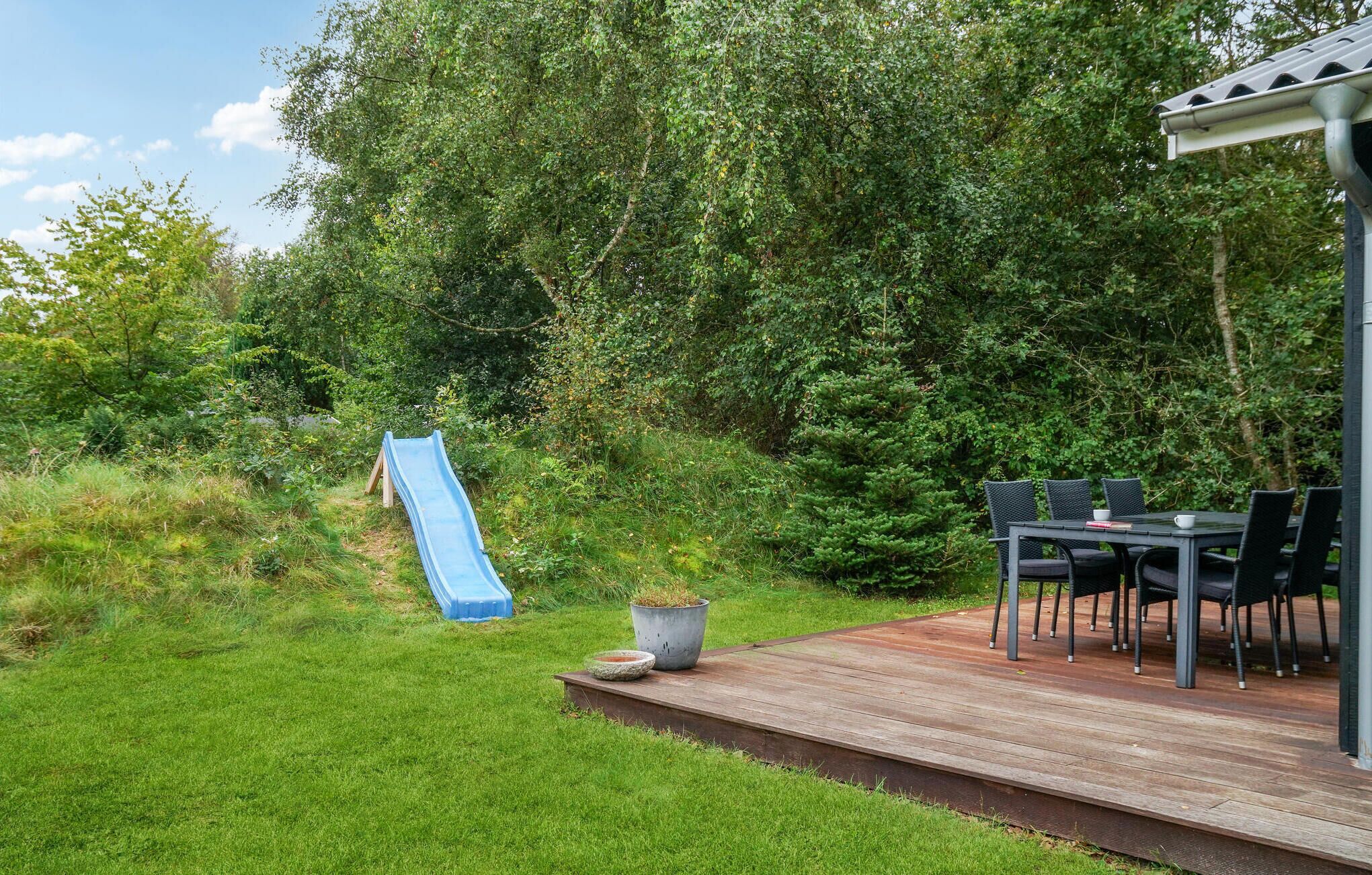 Un giardino sul retro con un patio in legno, uno scivolo blu e un tavolo con sedie.