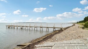 A wooden pier extending into calm waters, a pebble beach, and a clear sky.