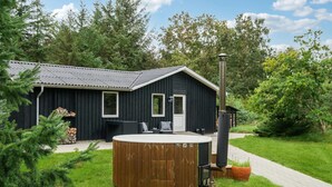 A wooden hot tub with a chimney, a black building with a metal roof, and a garden path.