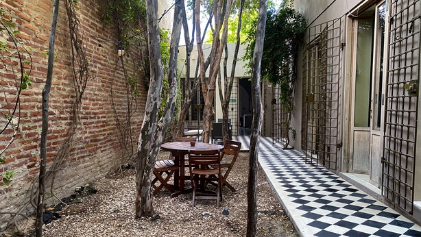 Un patio con suelo a cuadros, una mesa de madera con sillas y un muro de ladrillo.