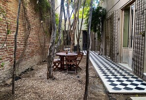 Un patio con suelo a cuadros, una mesa de madera con sillas y un muro de ladrillo.