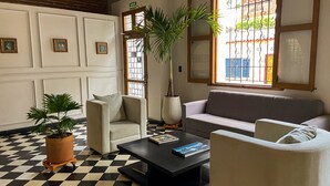 Una sala de estar con piso a cuadros, un sofá, un sillón, una mesa de centro y una planta en maceta.