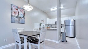 Una cocina moderna con armarios blancos, un refrigerador de acero inoxidable y un comedor con mesa de madera y sillas blancas.