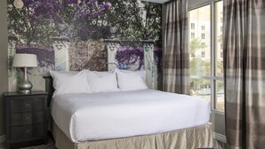 A neatly made bed with white linens, a dark nightstand with a lamp, and a wall mural with purple flowers. - 2 Bed 2 Bath Las Vegas - Pools, Hot Tubs, Cabanas and More! (Las Vegas)