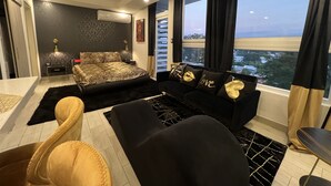 Camera moderna con un letto grande, un divano nero e vista sulla città attraverso ampie finestre.