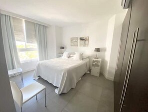Quarto moderno com cama, mesas de cabeceira, escrivaninha e uma cadeira.