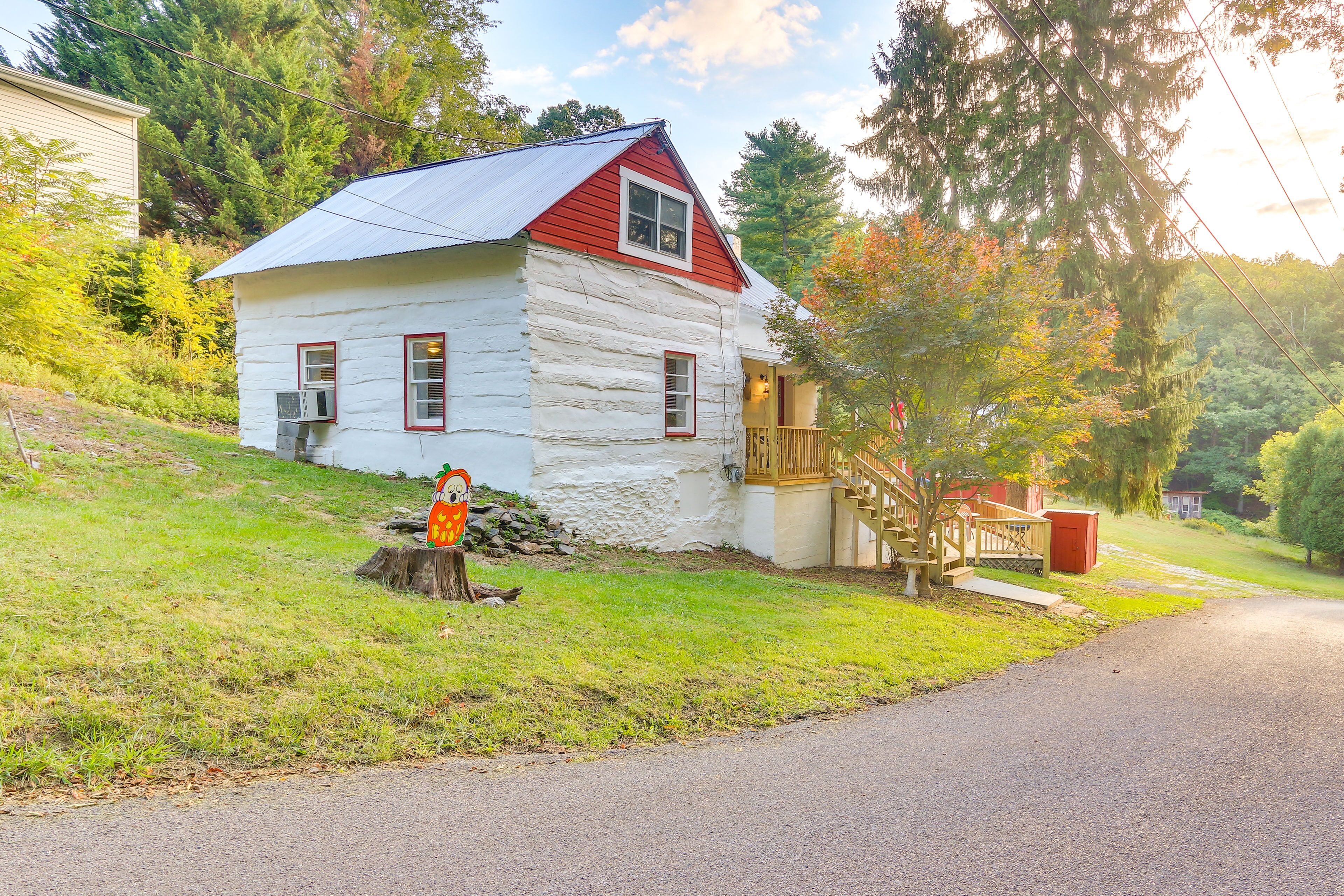 A log cabin with a red roof and white walls, a wooden deck, and a staircase leading to a porch.