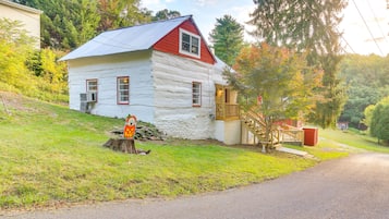 A log cabin with a red roof and white walls, a wooden deck, and a staircase leading to a porch.