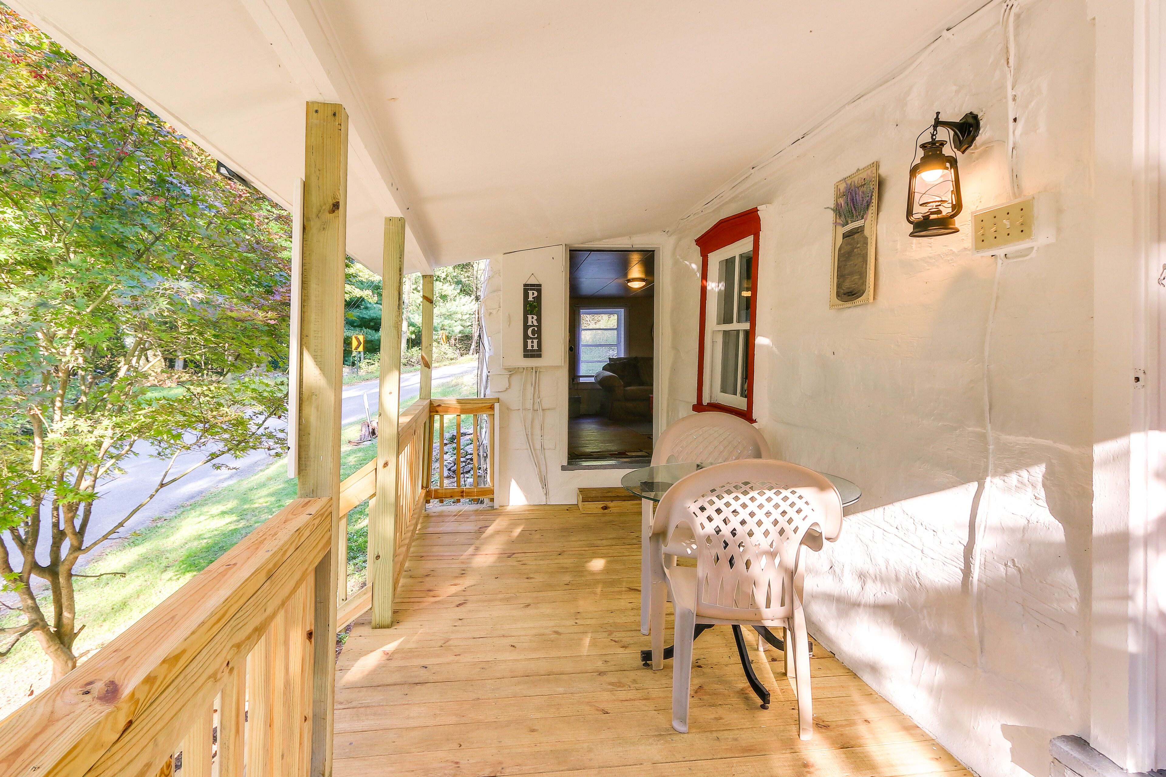 A wooden porch with a white chair, a small table, and a view of a road and greenery.