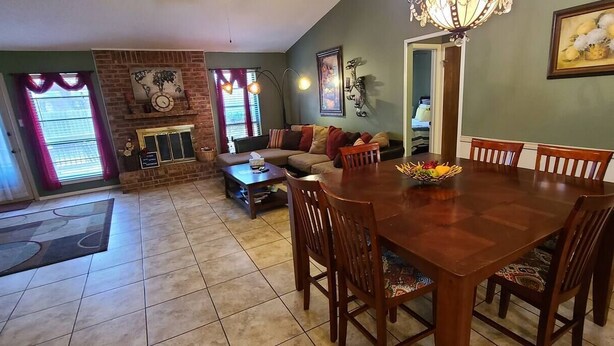 A spacious living room with a fireplace, a dining area with a wooden table and chairs, and a kitchen visible in the background. - Family-sized home with quick access to the loop!! (Midland)