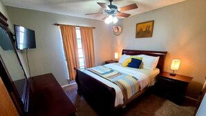 A bedroom with a bed, a ceiling fan, a TV, and a painting on the wall. - Family-sized home with quick access to the loop!! (Midland)
