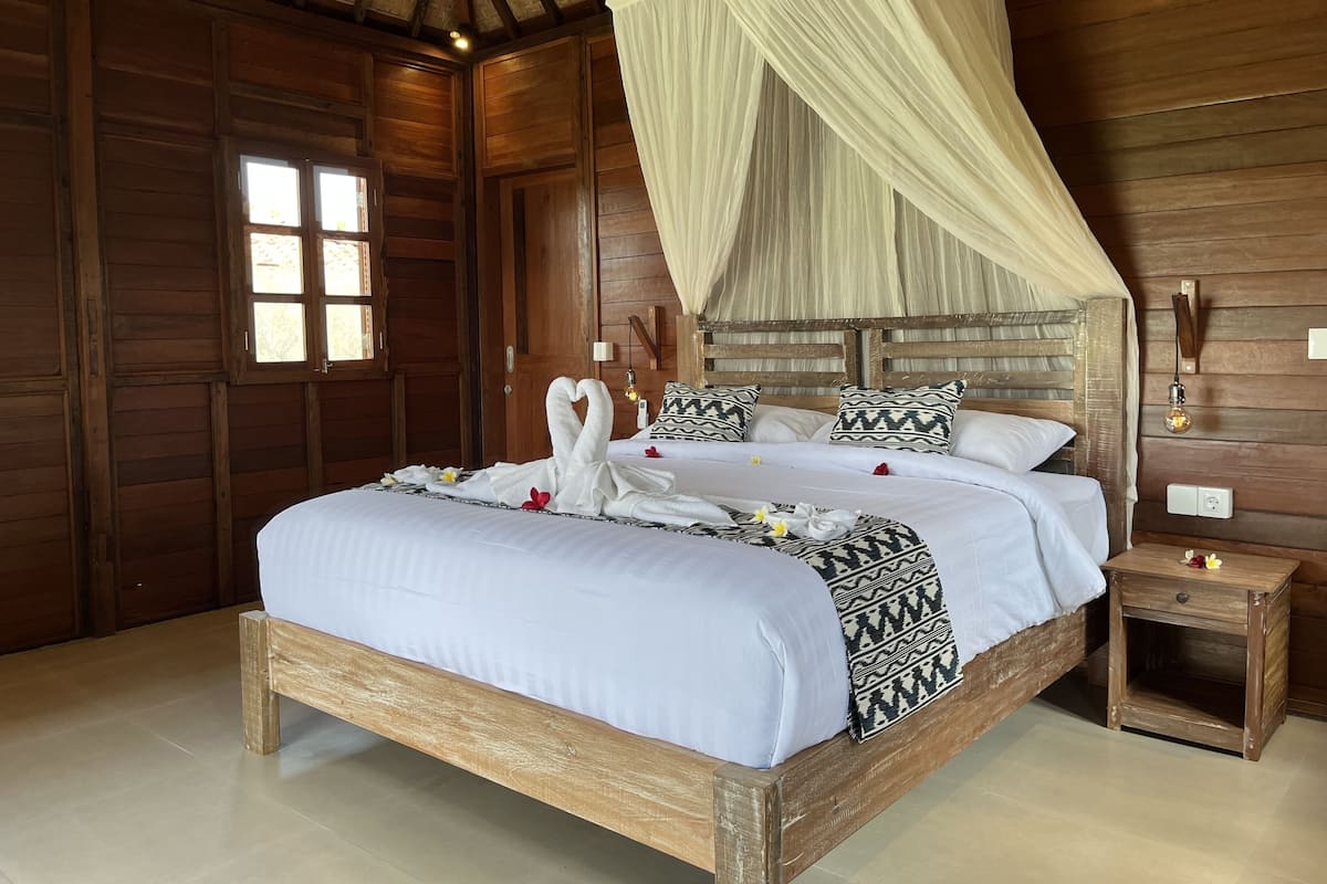 A wooden room with a bed, a nightstand, and a window.
