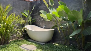Un baño exterior moderno con una bañera independiente, rodeado de exuberante vegetación tropical y una estructura de pérgola.